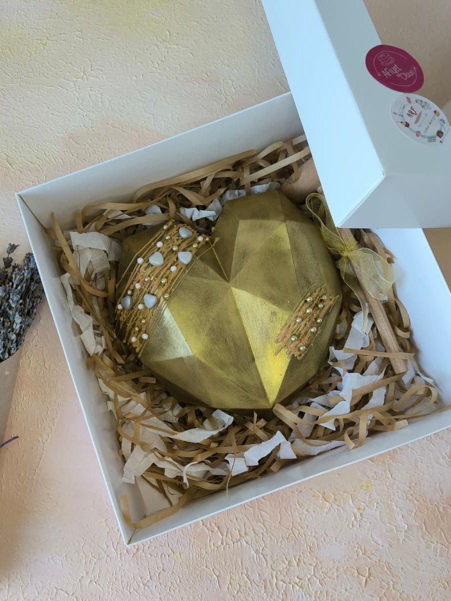 Hediye kutusunda, kâğıt dolgu üzerinde, altın rengi geometrik çikolata kalp pinyata ve tahta çekici